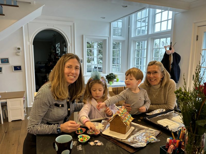 Three generations decorating a gingerbread house together